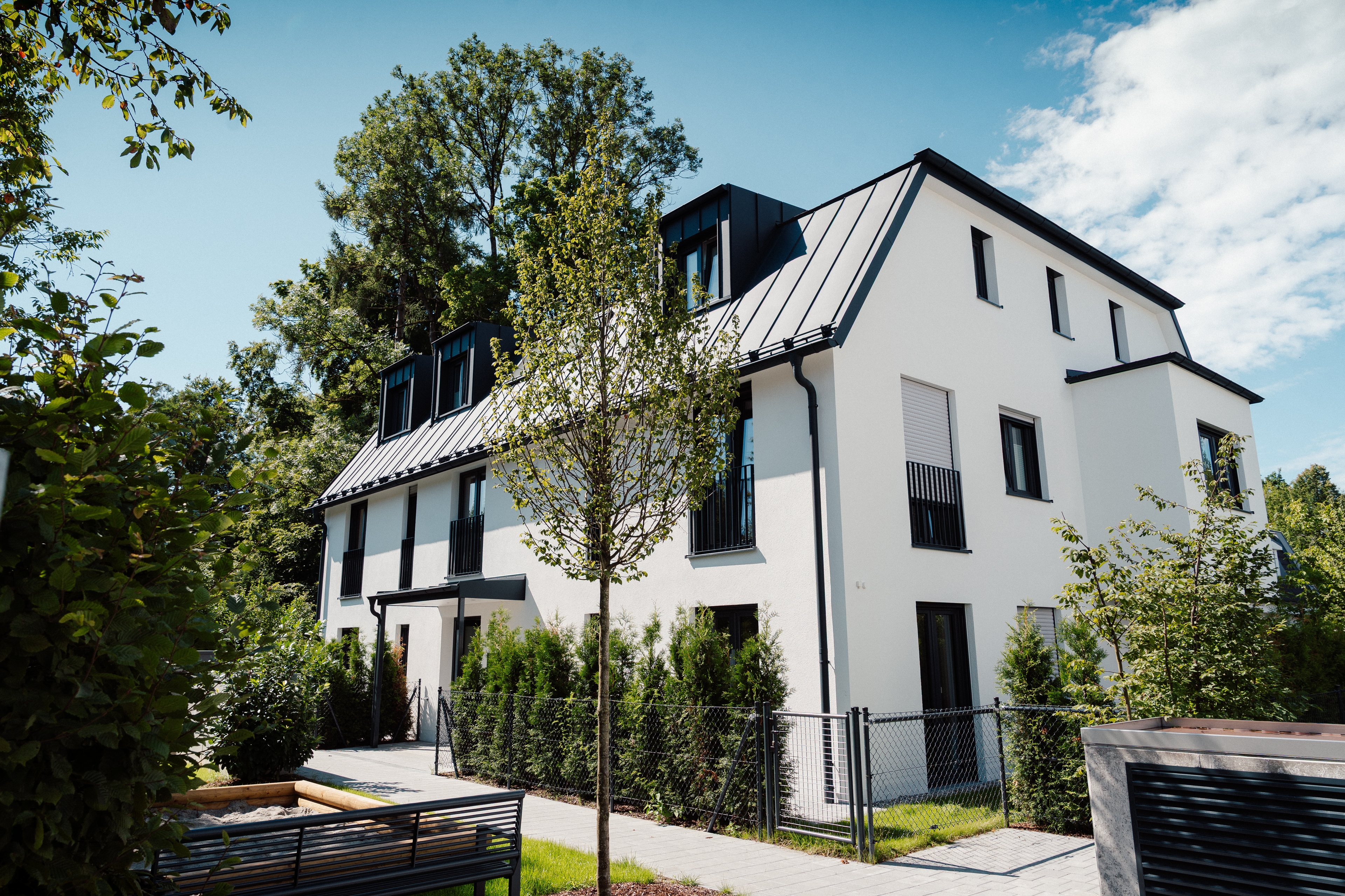 Sperberstraße 42 – Mehrfamilienhaus mit weißer Fassade und schwarzem Satteldach, Gartenansicht mit Weg und Hecken