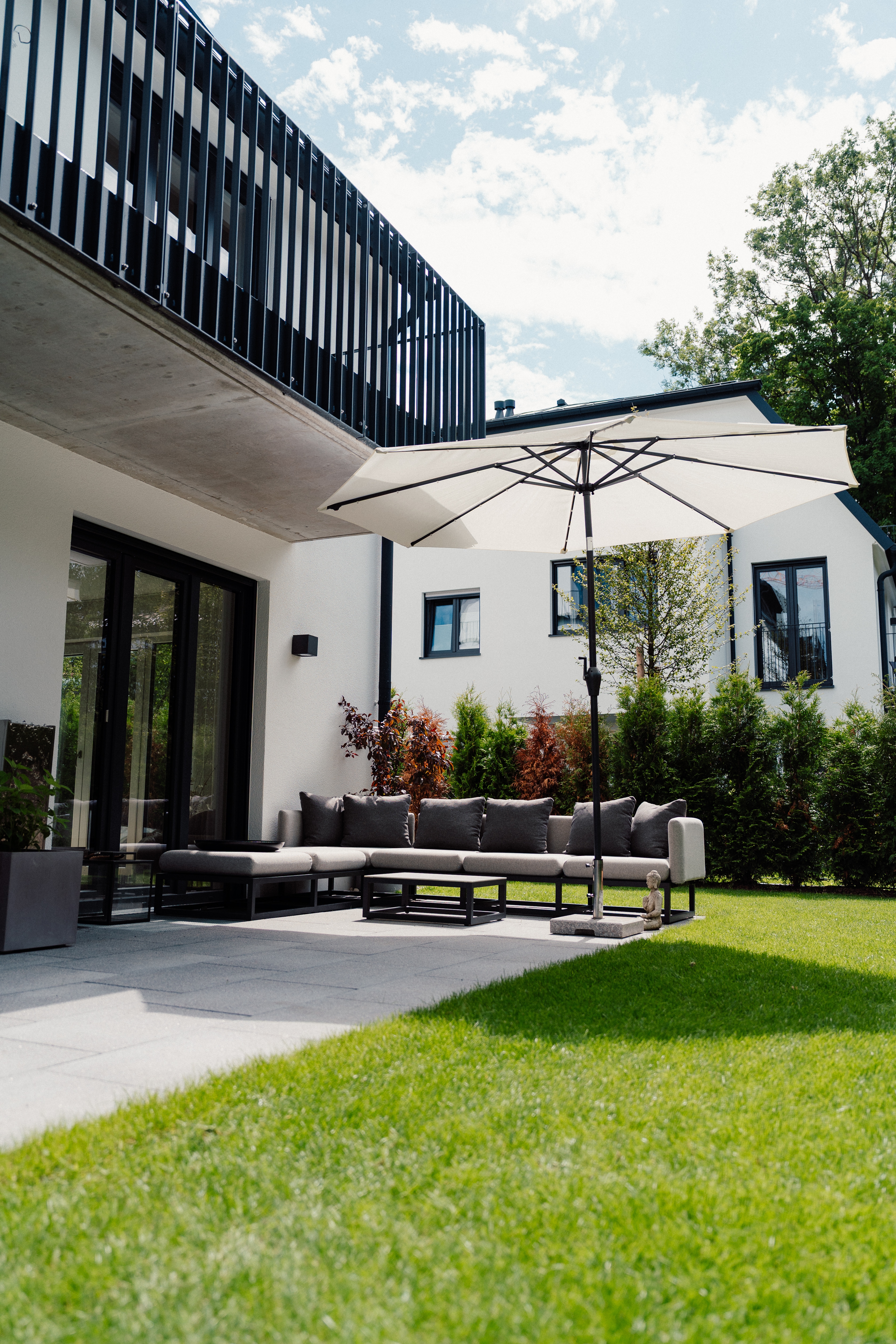 Terrasse mit Sitzgruppe und großem Sonnenschirm vor modernem Haus, Rasen im Vordergrund
